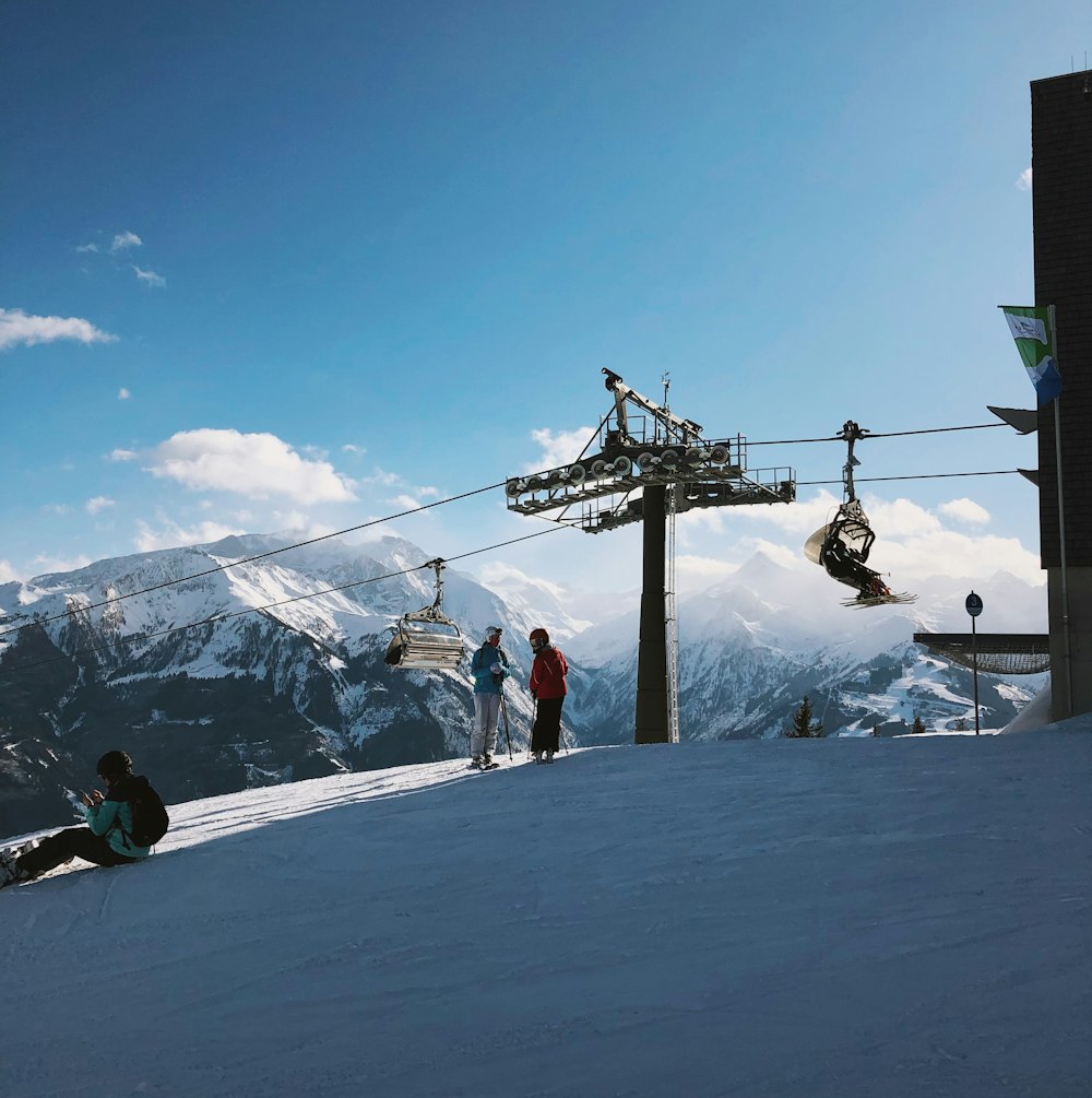 person in red jacket and blue pants riding ski lift over snow covered mountain during daytime