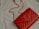 A red quilted leather handbag with a gold chain strap and metallic logo accent rests on a light-colored fabric surface.