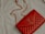 A red quilted leather handbag with a gold chain strap and metallic logo accent rests on a light-colored fabric surface.
