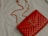 A red quilted leather handbag with a gold chain strap and metallic logo accent rests on a light-colored fabric surface.
