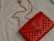 A red quilted leather handbag with a gold chain strap and metallic logo accent rests on a light-colored fabric surface.