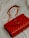 A luxurious red leather handbag with a quilted pattern and a prominent gold logo. The bag features a gold chain strap and is placed on a soft, light-colored fabric background.