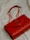 A luxurious red leather handbag with a quilted pattern and a prominent gold logo. The bag features a gold chain strap and is placed on a soft, light-colored fabric background.