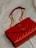 A luxurious red leather handbag with a quilted pattern and a prominent gold logo. The bag features a gold chain strap and is placed on a soft, light-colored fabric background.