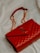 A luxurious red leather handbag with a quilted pattern and a prominent gold logo. The bag features a gold chain strap and is placed on a soft, light-colored fabric background.