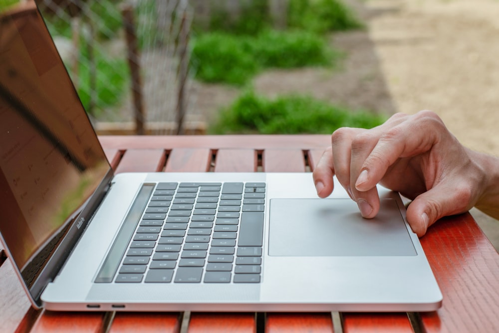 person using macbook air on brown wooden table during daytime