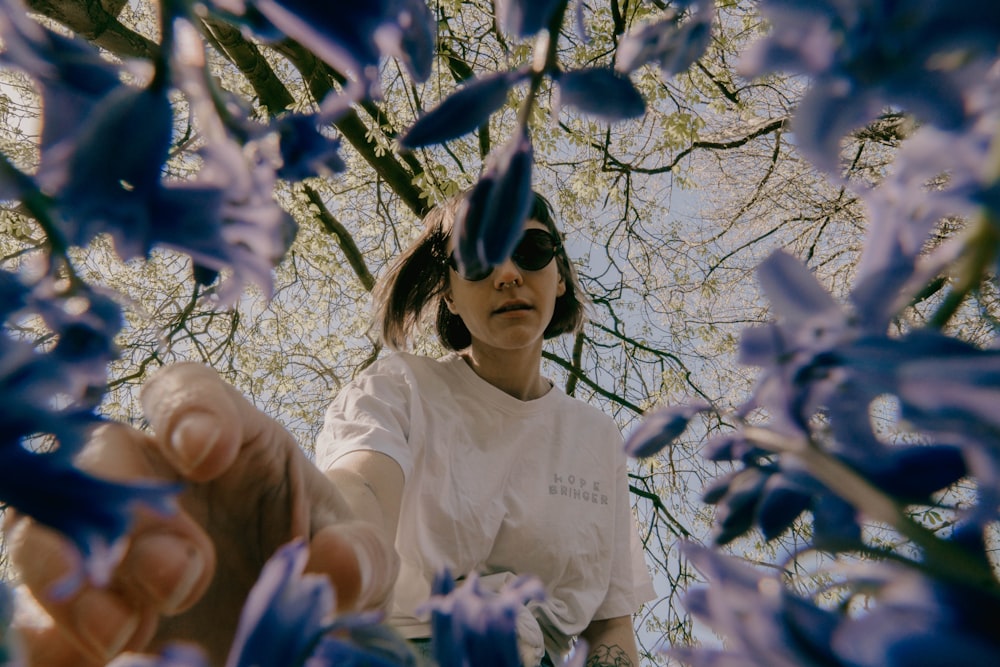 a woman in a white t - shirt holding up a purple flower