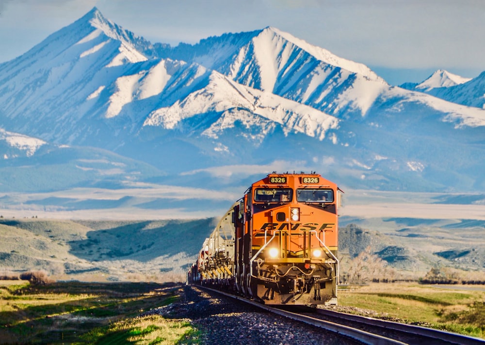 yellow train on green grass field near snow covered mountain during daytime