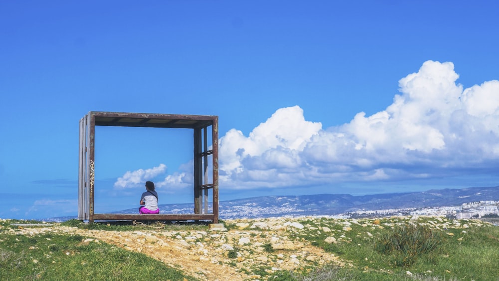 person sitting on brown wooden bench looking at the mountains during daytime