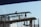 Construction workers are standing on a scaffold, installing steel reinforcement bars on a building under construction. The workers are equipped with safety gear, including helmets and harnesses, while carefully maneuvering the bars into place.
