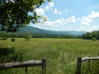 green grass field near green mountains under white clouds and blue sky during daytime