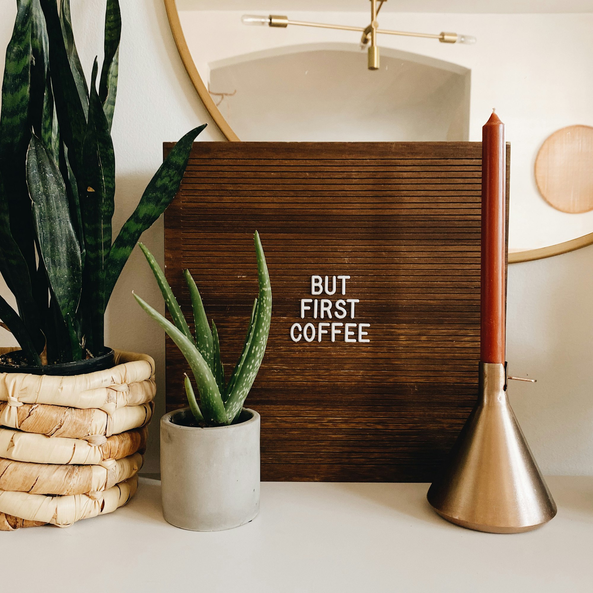 but first coffee letter board sign with candle stick and plants with round mirror and hanging west elm light in the background