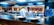 A commercial kitchen setting with chefs in white uniforms and black hats working at the counter. The kitchen is equipped with shiny metal bowls, cooking pots, and utensils. The background features a wall adorned with vibrant photographs of musicians.