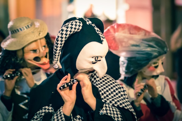 Several people are wearing colorful and elaborate costumes and masks that resemble traditional or theatrical characters. They are playing small flutes and appear to be participating in a festive event or parade.