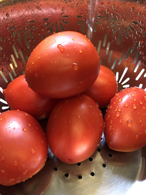 Close-up of a stainless steel tomato processing machine with ripe tomatoes being peeled.