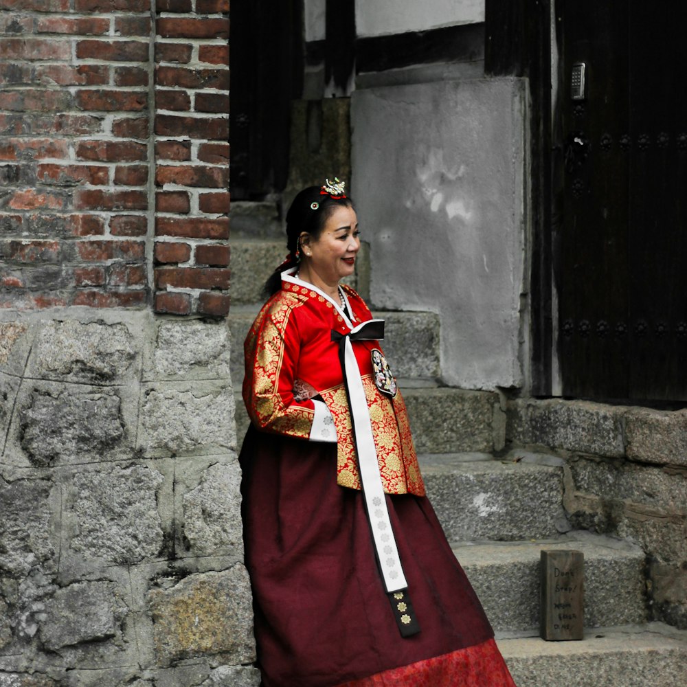 Donna in sari rosso e giallo in piedi accanto al muro di cemento grigio durante il giorno