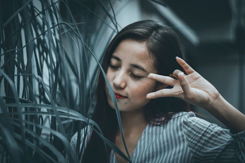 A young woman meditating peacefully under a large tree with soft green leaves.