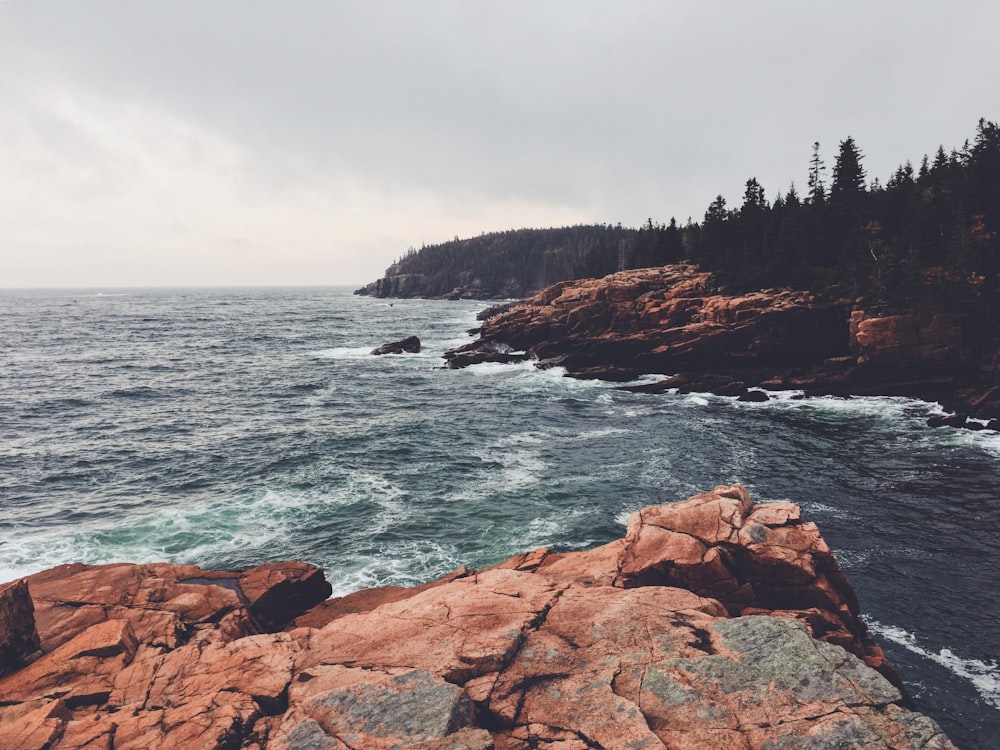 brown rocky mountain beside body of water during daytime