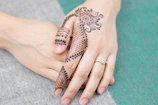 Close-up of a bride’s hands adorned with detailed henna patterns featuring floral and paisley motifs in deep maroon.