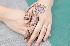 Close-up of a bride’s hands adorned with detailed henna patterns featuring floral and paisley motifs in deep maroon.
