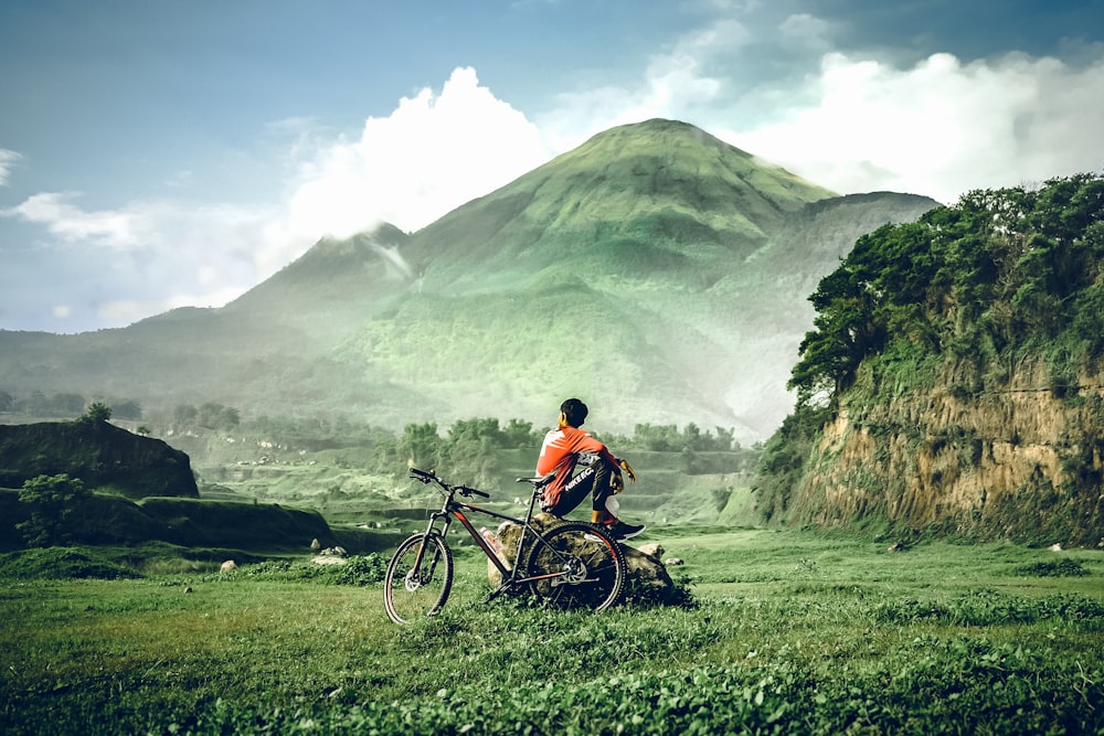 man in orange shirt riding red and black mountain bike on green grass field during daytime