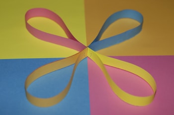 Four loops of colorful paper strips intersect at the center, arranged on a background divided into four quadrants of blue, yellow, pink, and yellow colors.