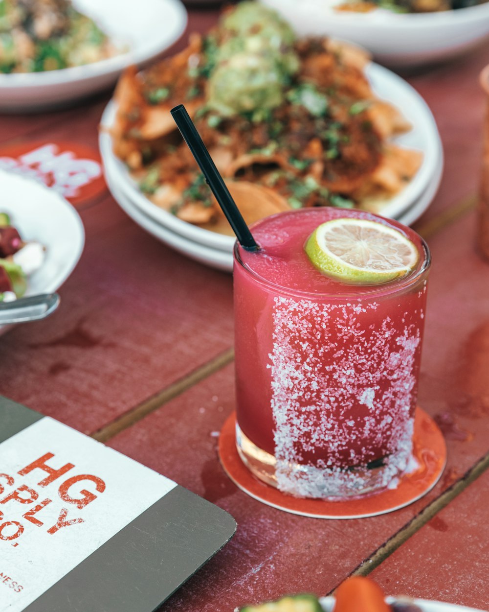 clear drinking glass with red liquid and black straw on red table