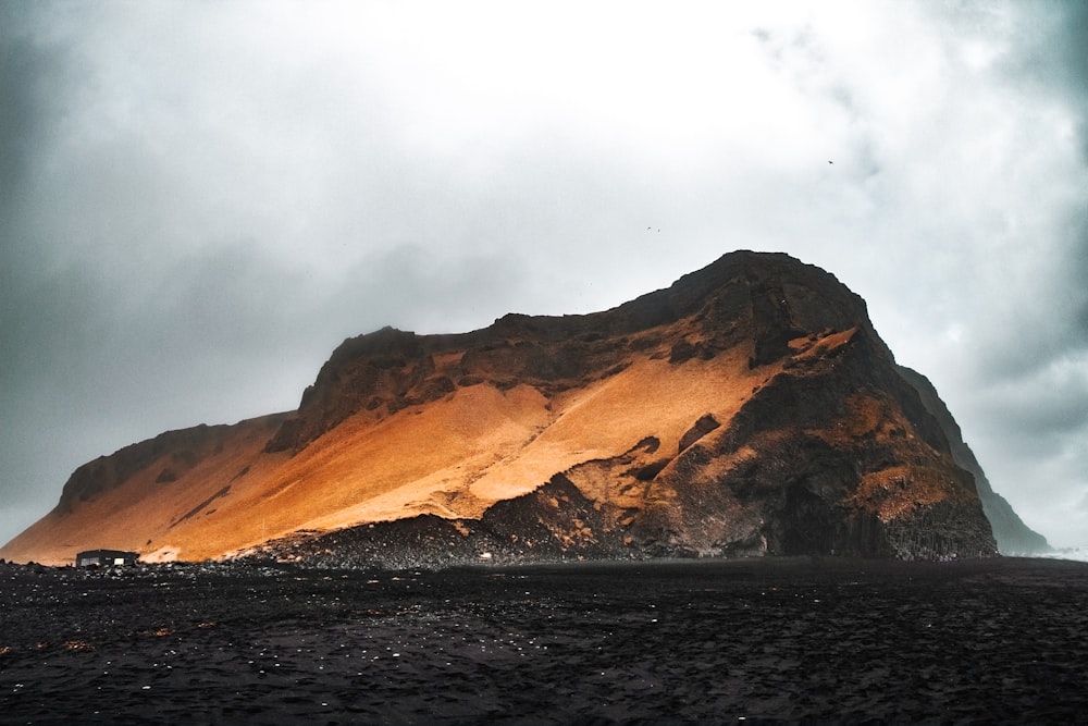 brown mountain near body of water under cloudy sky during daytime