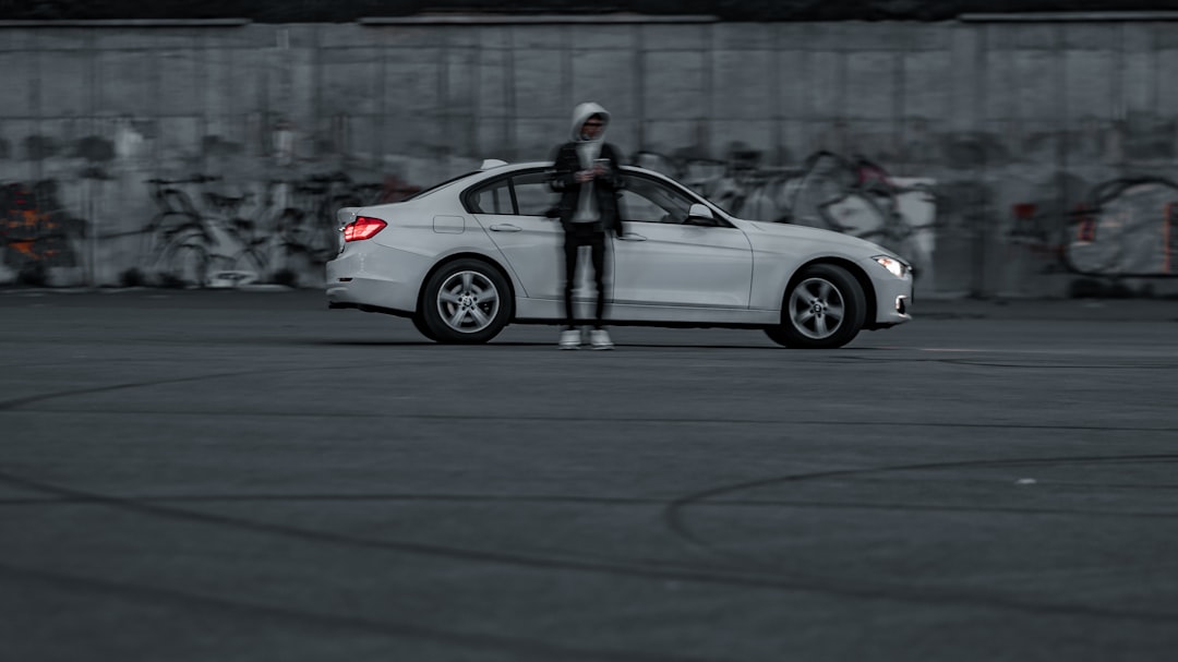 man in black jacket and black pants standing beside white sedan