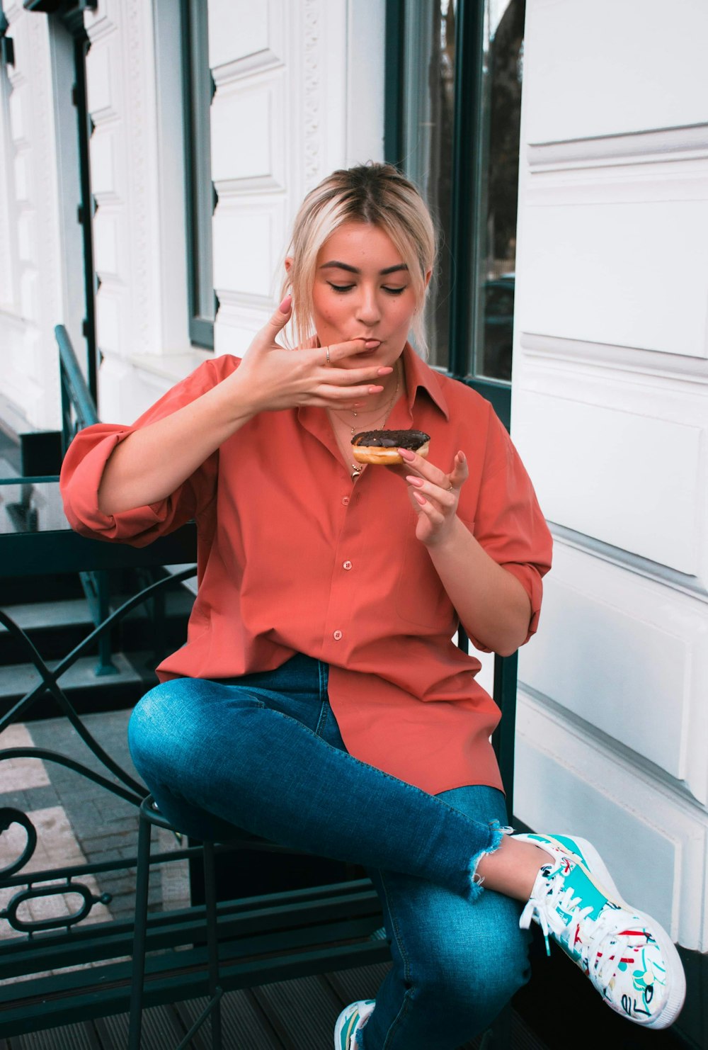 Frau in rosa Hemd und blauer Jeans sitzt auf schwarzem Metallstuhl