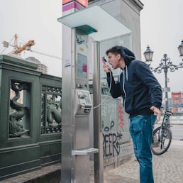 man in black jacket and blue denim jeans standing near black telephone booth during daytime