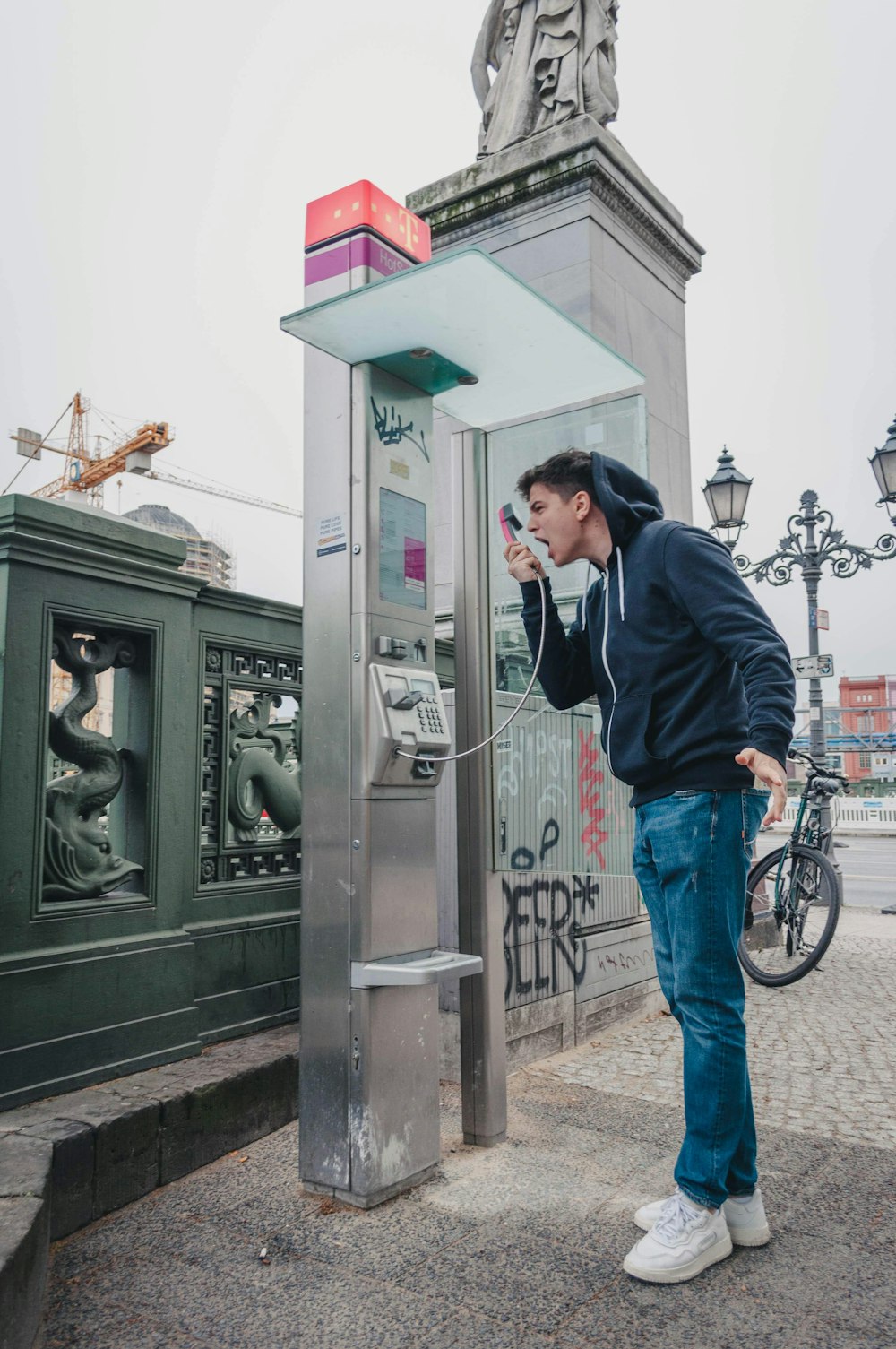 uomo in giacca nera e jeans blu in piedi vicino alla cabina telefonica nera durante il giorno