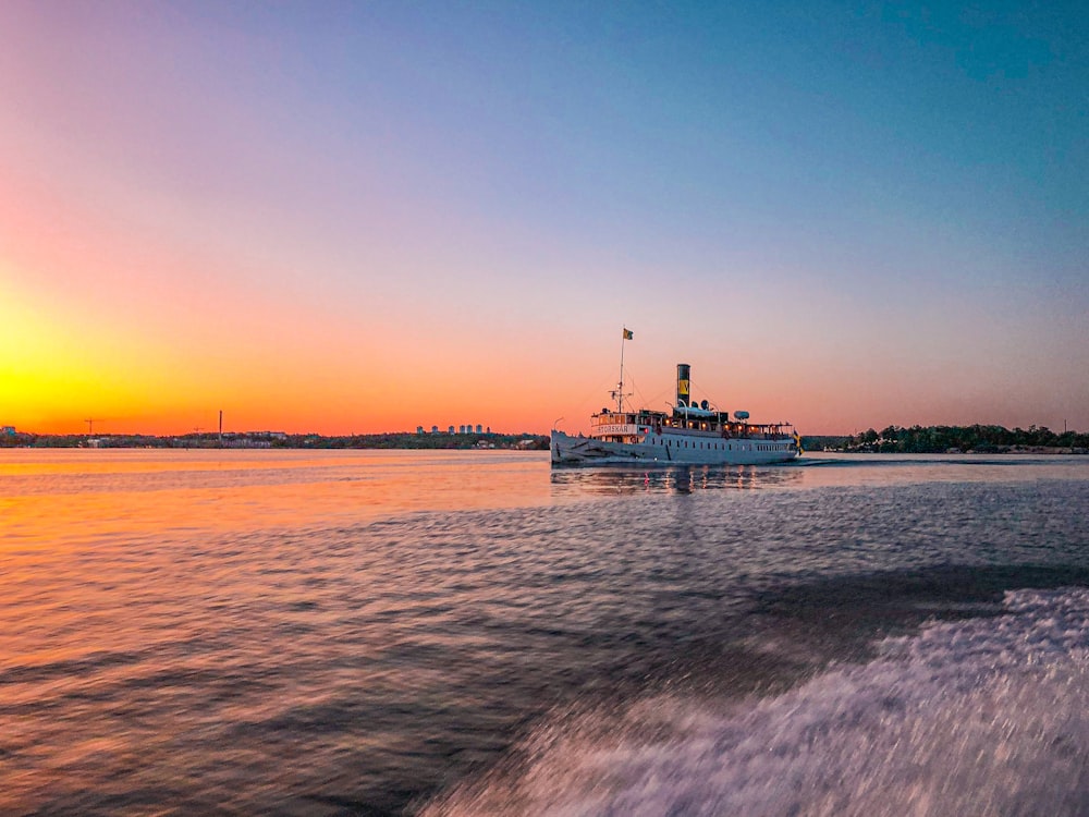 blue and white ship on sea during sunset