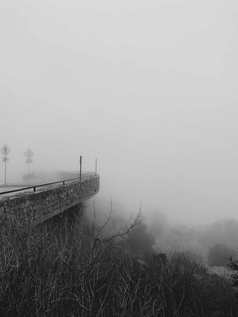 grayscale photo of person standing on bridge