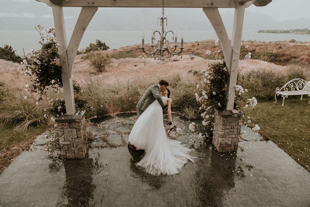 bride and groom kissing under brown wooden bridge during daytime