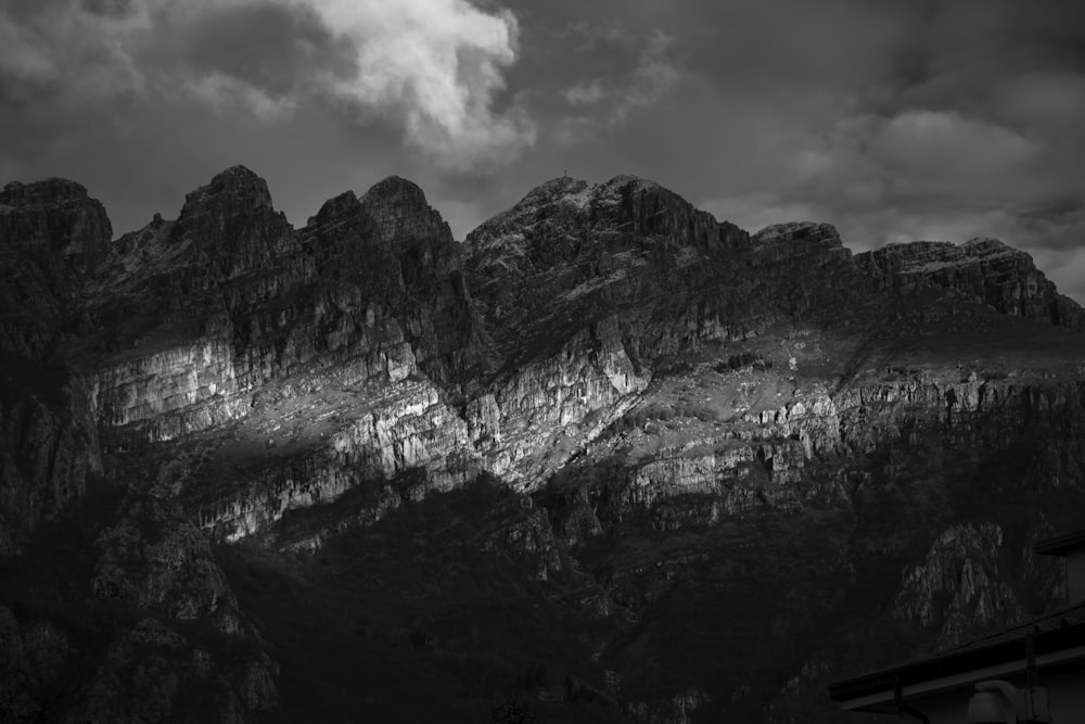 grayscale photo of rocky mountain under cloudy sky