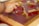 A hand is manipulating pieces of tape on a surface covered with red and yellow paint. The surface appears to be a glass or plastic sheet held in a wooden frame.