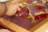A hand is manipulating pieces of tape on a surface covered with red and yellow paint. The surface appears to be a glass or plastic sheet held in a wooden frame.