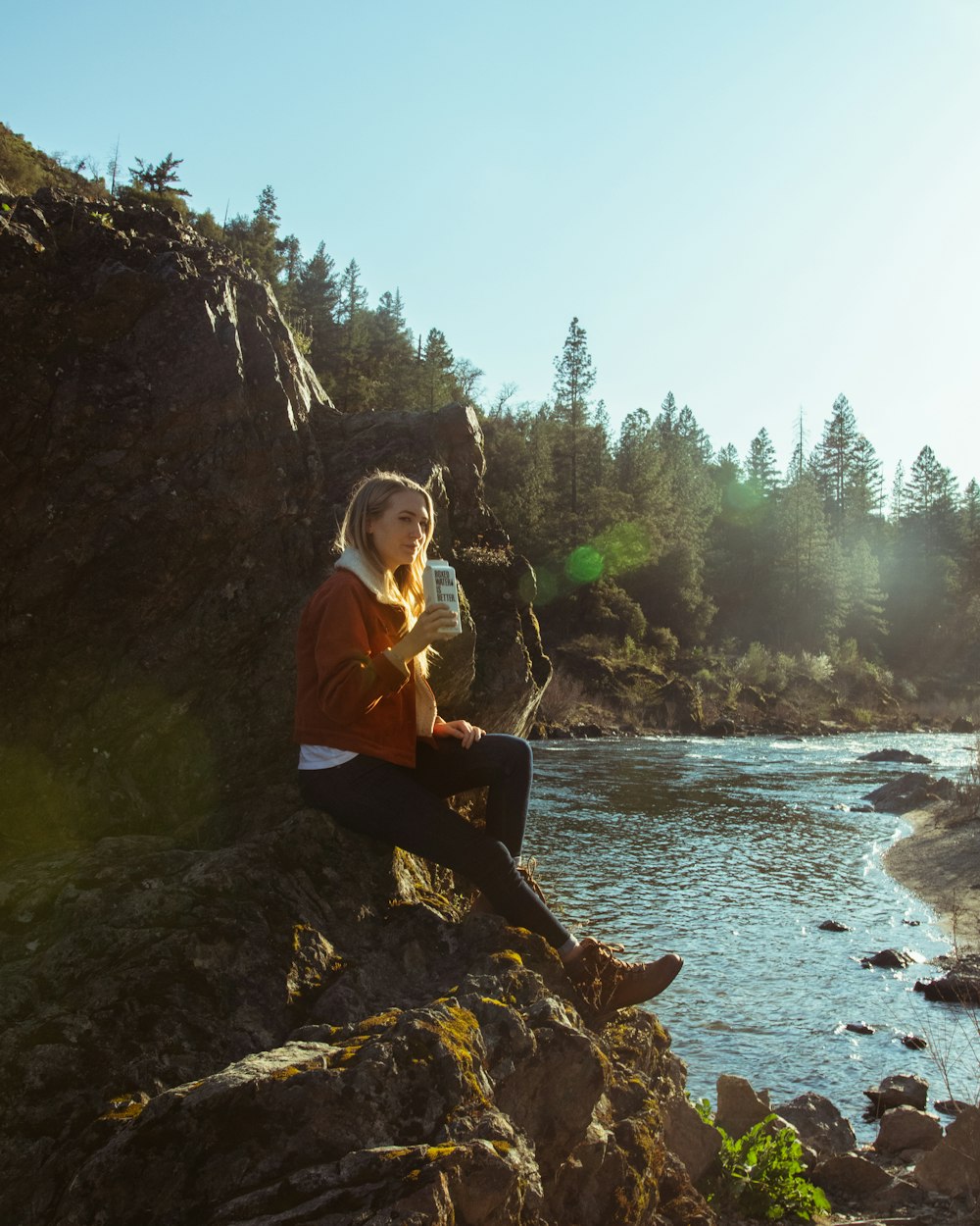 woman in blue long sleeve shirt sitting on rock near river during daytime