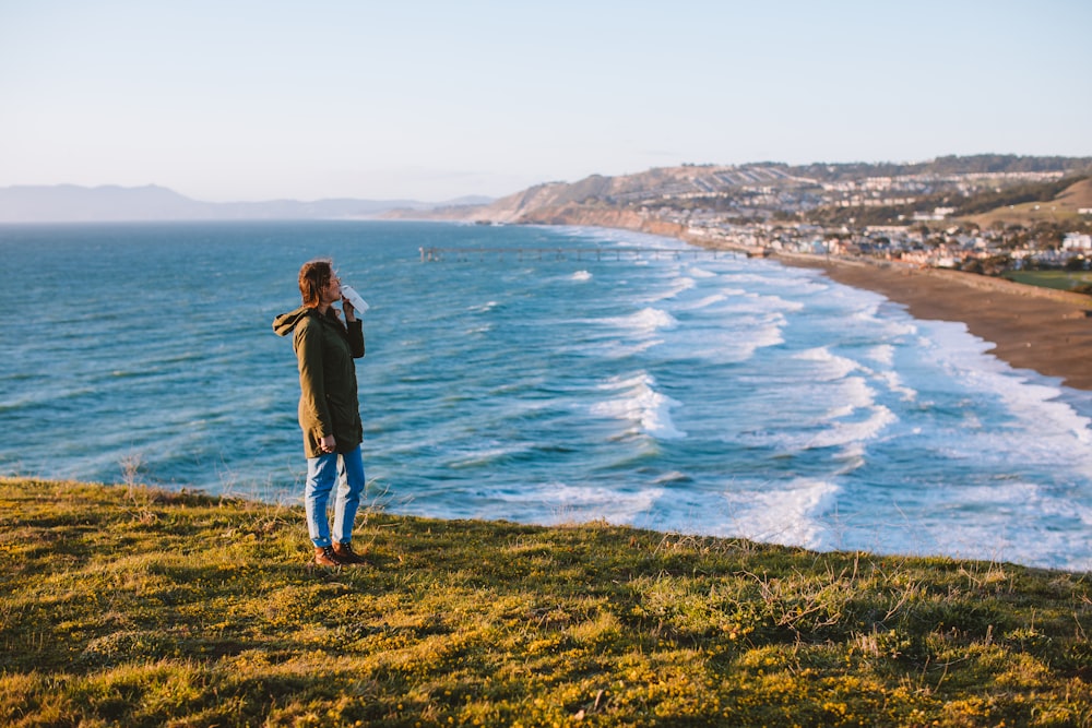 woman in black jacket and blue denim jeans standing on green grass field near body of on on on with