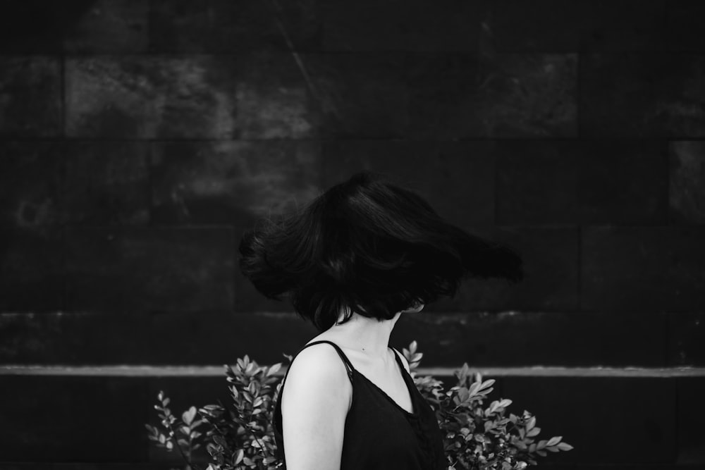 woman in black tank top standing near flowers in grayscale photography