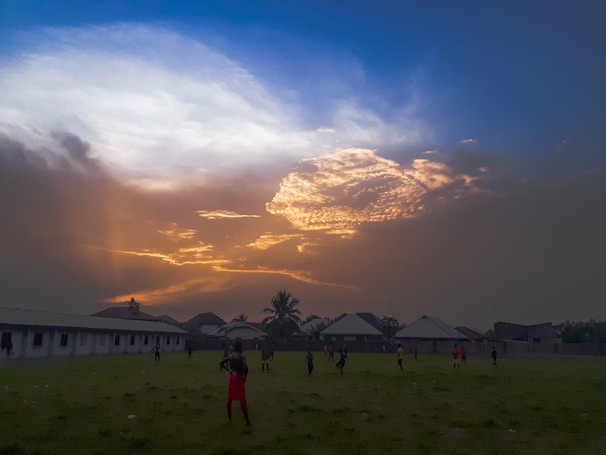 Children laughing and playing soccer on a turquoise-to-blue gradient field at sunset.