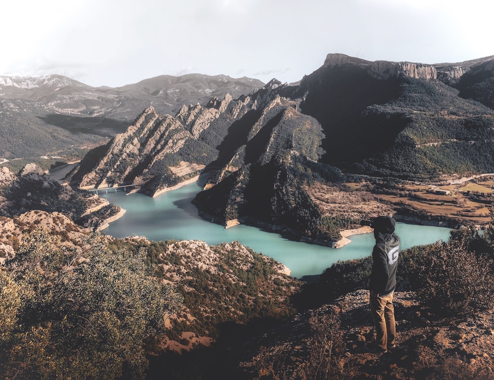 man in white shirt and black pants standing on brown rock formation near lake during daytime