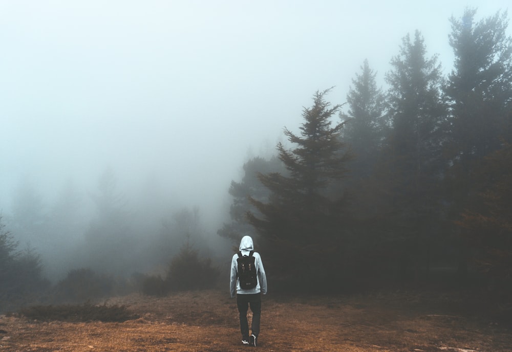 person in white jacket standing on brown field surrounded by green trees