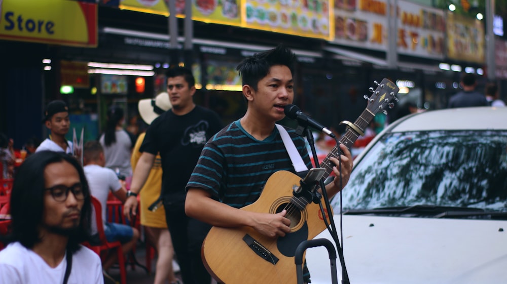 man in black and blue striped shirt playing brown acoustic guitar