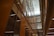 A modern interior featuring high ceilings and rows of glass-panelled walls, creating a spacious, well-lit corridor. The architectural design incorporates clean lines, with balconies and lighting fixtures enhancing the sense of openness.