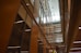 A modern interior featuring high ceilings and rows of glass-panelled walls, creating a spacious, well-lit corridor. The architectural design incorporates clean lines, with balconies and lighting fixtures enhancing the sense of openness.
