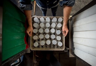 person in black shirt and blue denim jeans standing in front of white plastic bottles