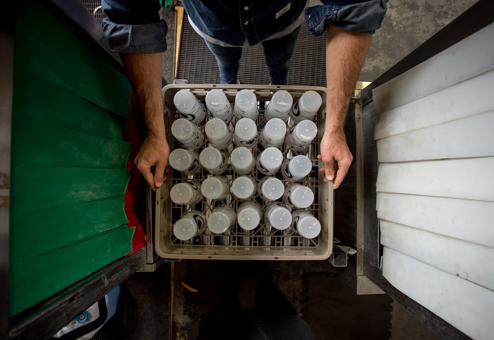 person in black shirt and blue denim jeans standing in front of white plastic bottles