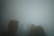 Silhouettes of several people are seen through a dense fog, creating a mysterious and eerie atmosphere. The figures are mostly indistinct, with traces of facial features and hairstyles barely discernible against the misty backdrop.